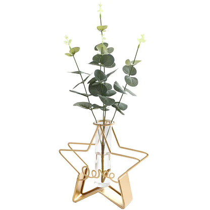 Gold star-shaped vase with a clear glass base holding green leaves on a white background
