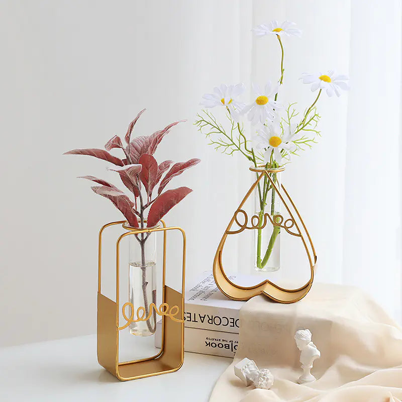 Two decorative vases with gold frames holding plants on a white surface.