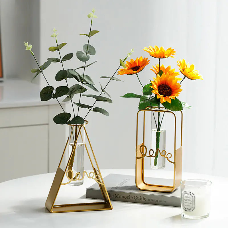 Two gold geometric vases with plants on a white surface