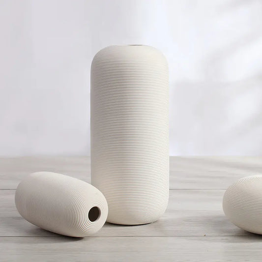 Three cylindrical ceramic vases with textured surfaces on a light wooden surface.