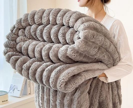 Person holding a large, fluffy gray blanket indoors.