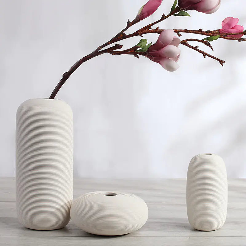 Set of three white ceramic vases with a branch of pink flowers on a light background