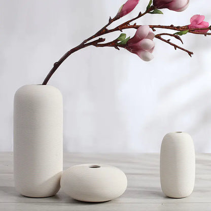 Set of three white ceramic vases with a branch of pink flowers on a light background