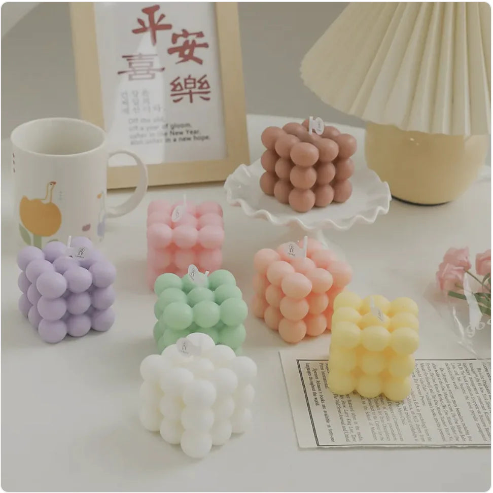 Colorful bubble-shaped candles on a table with a mug and lamp in the background.