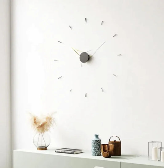 Modern wall clock on a white wall with decorative items on a shelf below.