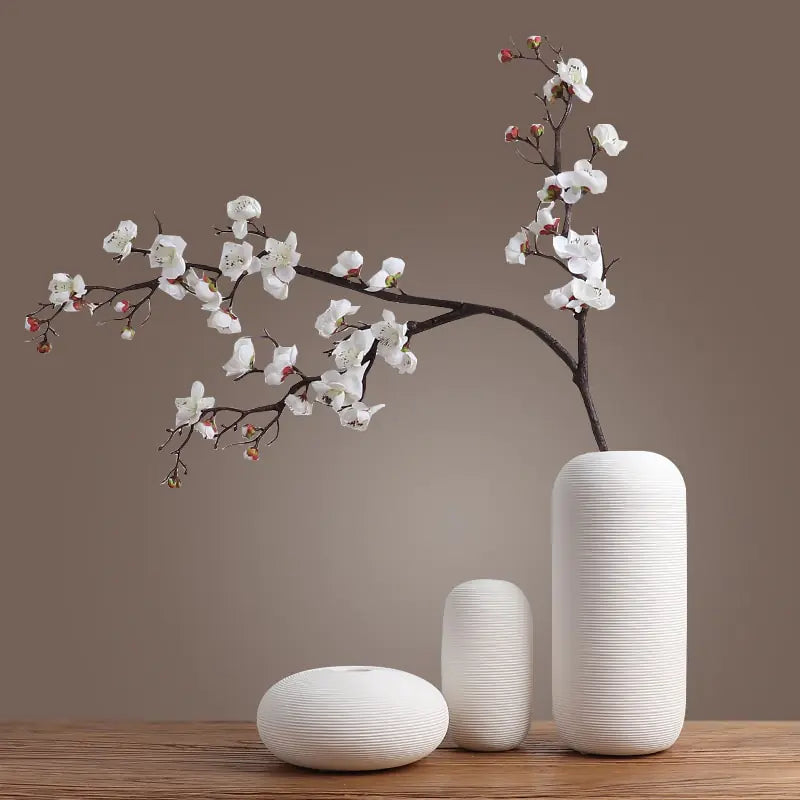 Three white textured vases with a branch of white flowers on a brown background
