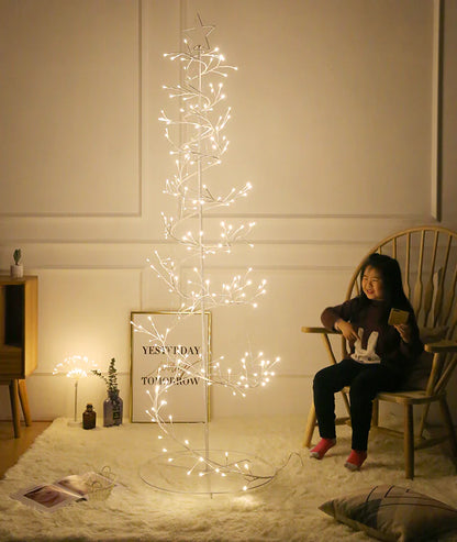 Woman sitting next to a decorative light tree in a room with a white wall and wooden furniture.