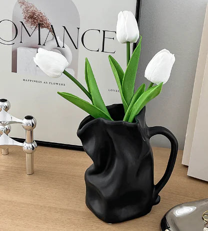 Black pitcher vase with white tulips on a wooden surface