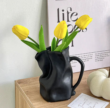 Black pitcher vase with yellow tulips on a wooden surface