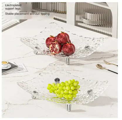 Clear glass fruit bowl with pomegranates and grapes on a marble surface